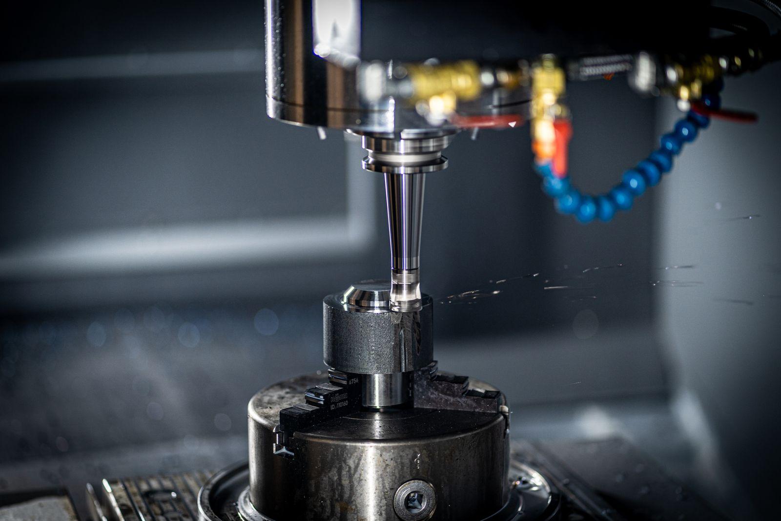 CNC milling machine tool positioned over a metal workpiece held in a three-jaw chuck