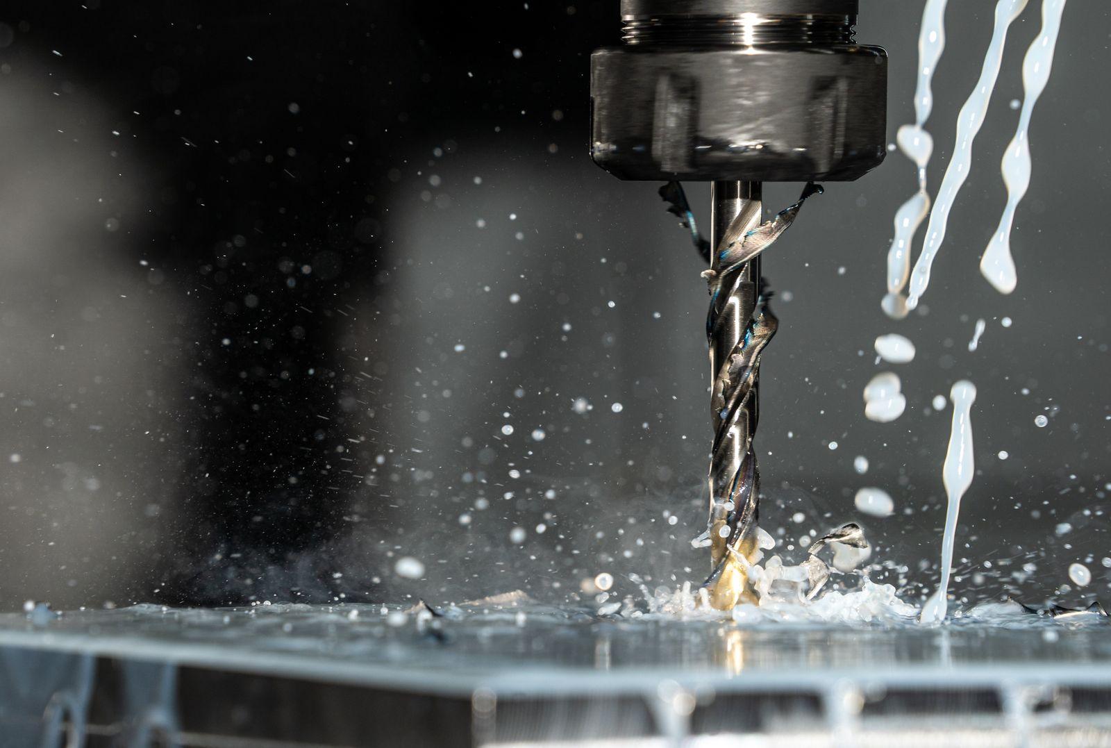 Drill bit cutting into a metal workpiece with flood coolant on a CNC machine